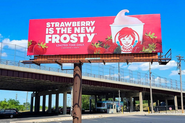 Reklame Billboard yang ada di tengah jalan berisi promosi makanan dan berwarna merah menarik